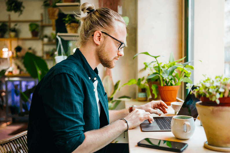 a man sits at a desk with a coffee mug using a laptop