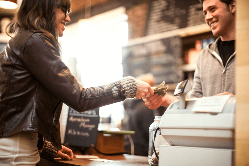 A female customer at a convenience store handing cash to a male cashier.