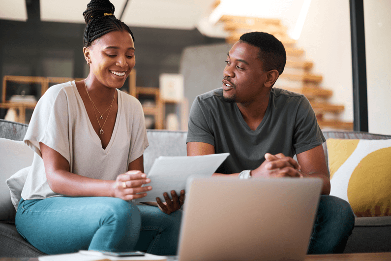 A couple sits on a couch and reviews how a savings account works and its benefits.