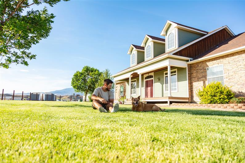 A man sits outside of his home with his dog on the lawn