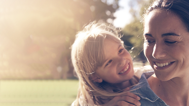 Young blonde girl smiles at woman with golden sunlight shining in the background.
